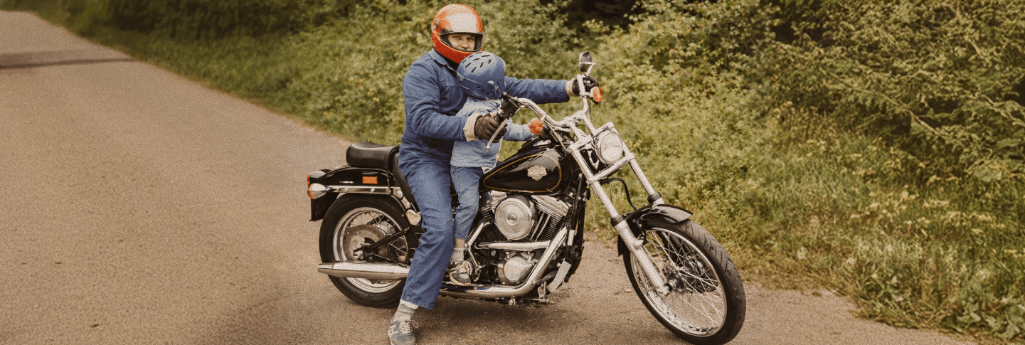 Person och barn åker motorcykel på landsväg omgiven av grönska